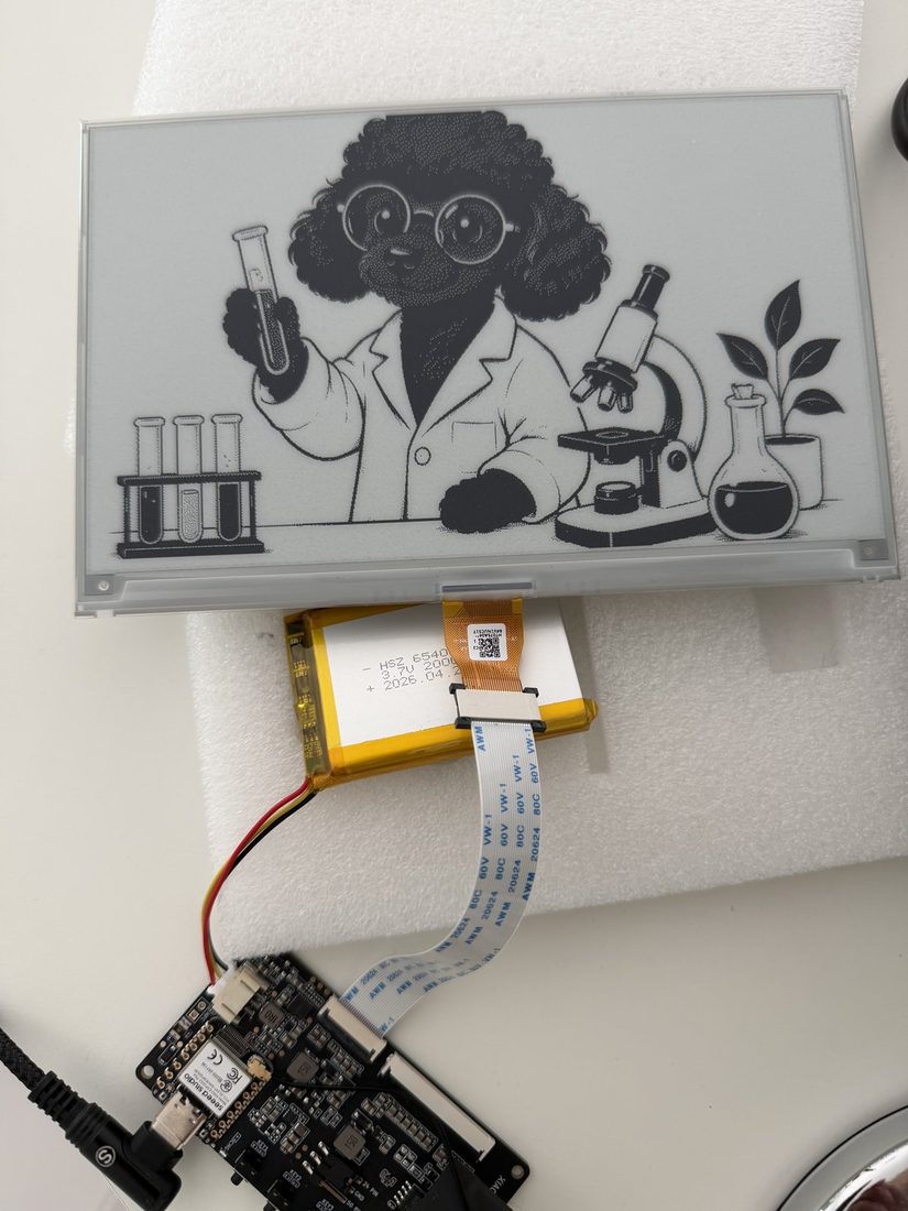 An e-paper panel, an ESP32 board and a battery, before assembly.